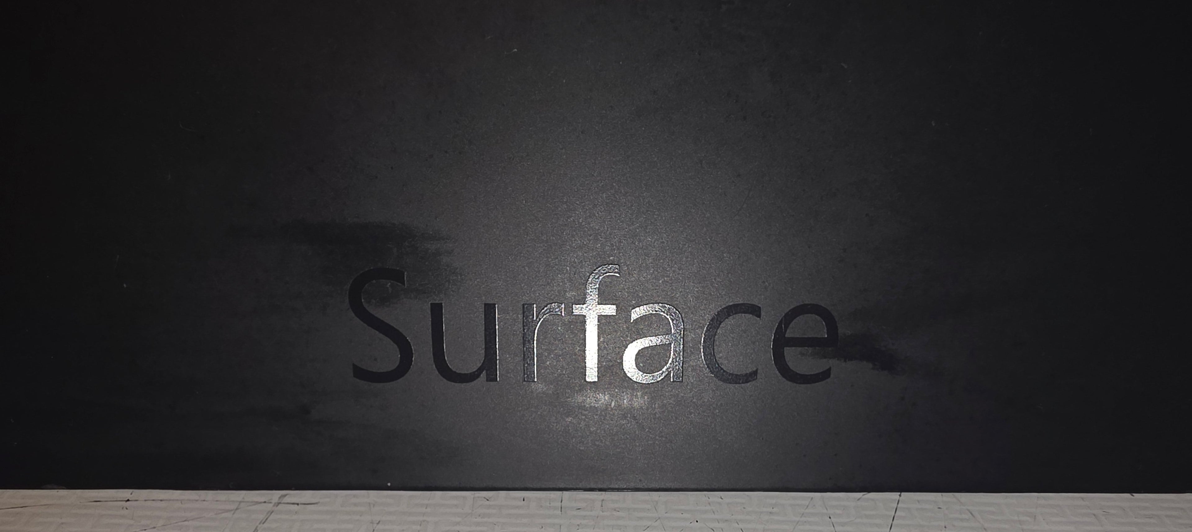 Black wall with 'Surface' branding above a white tiled floor.